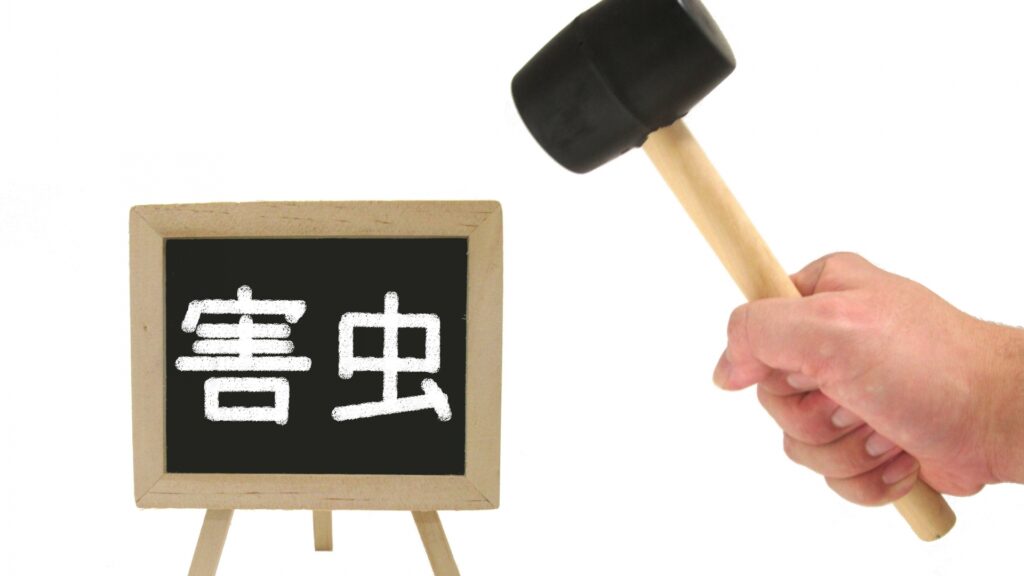 害虫と書かれた看板とハンマーをもつ手元